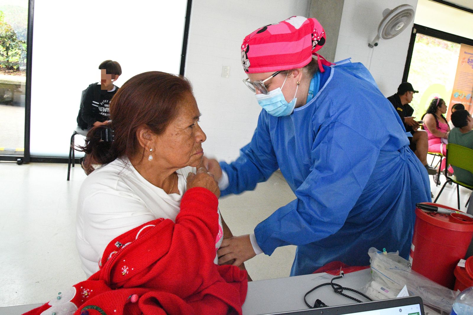 Mujer con bata azul vacuna a paciente mayo